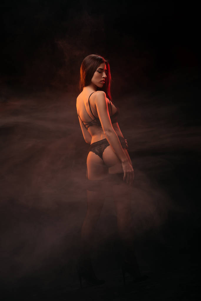 beautiful sensual young woman in black lingerie posing in dark smoky room - Photo, Image