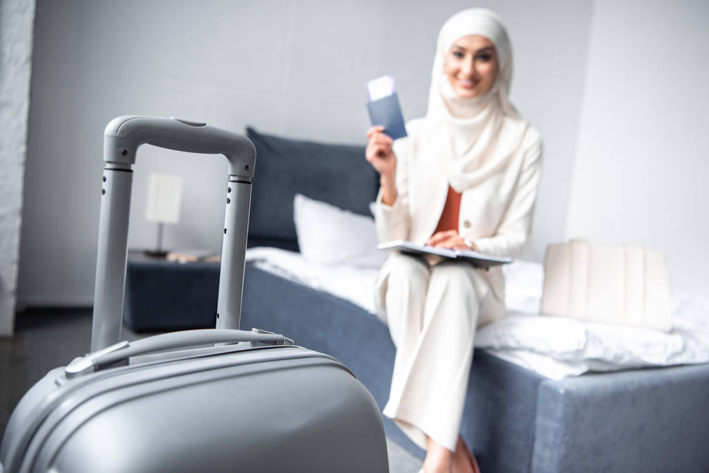 close-up view of suitcase and smiling muslim woman holding passport with boarding pass at home - Photo, Image