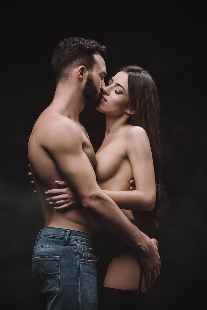 passionate boyfriend hugging and kissing nude girlfriend, isolated on black - Photo, Image