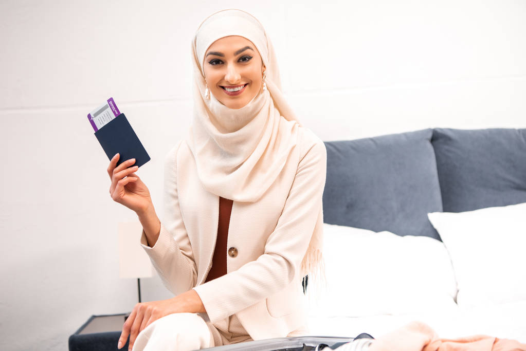 feliz joven musulmana mujer con pasaporte con tarjeta de embarque y sonriendo a la cámara
 - Foto, Imagen
