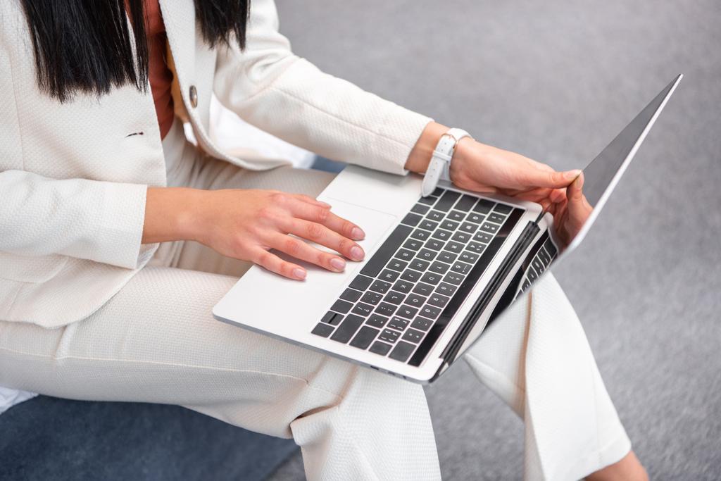 tiro recortado de mulher jovem em terno branco elegante usando laptop em casa
 - Foto, Imagem
