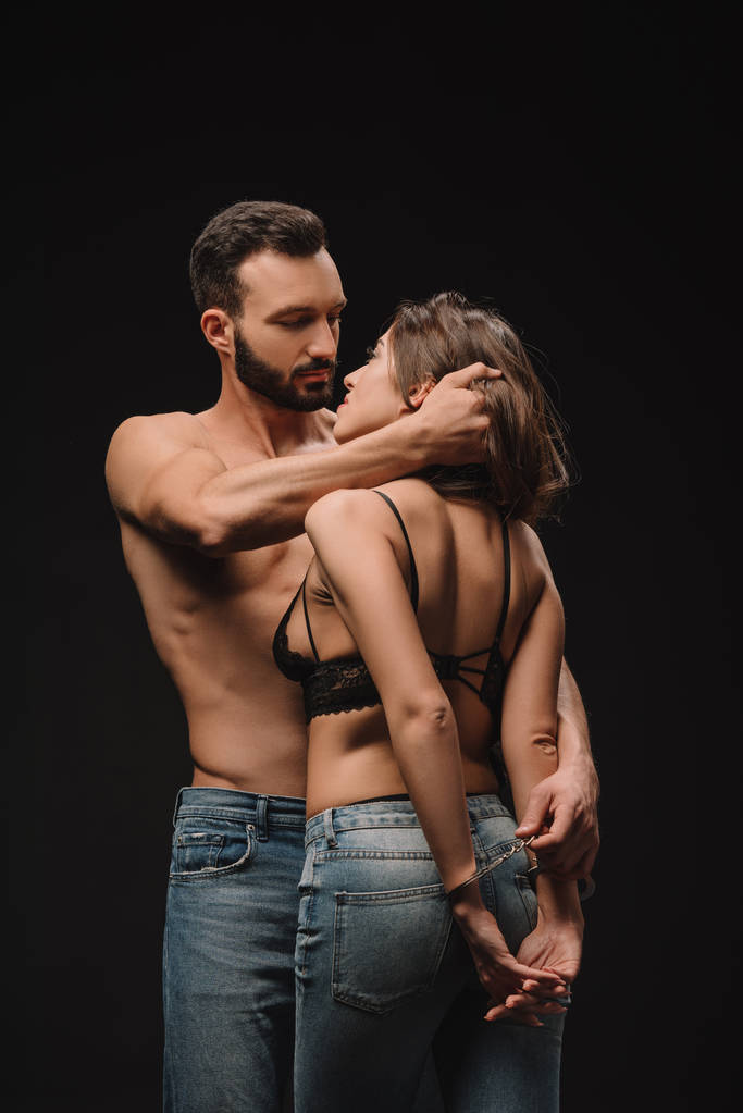 όμορφος shirtless άνδρας αγκαλιάζει σέξι γυναίκα με χειροπέδες που απομονώνονται σε μαύρο - Φωτογραφία, εικόνα