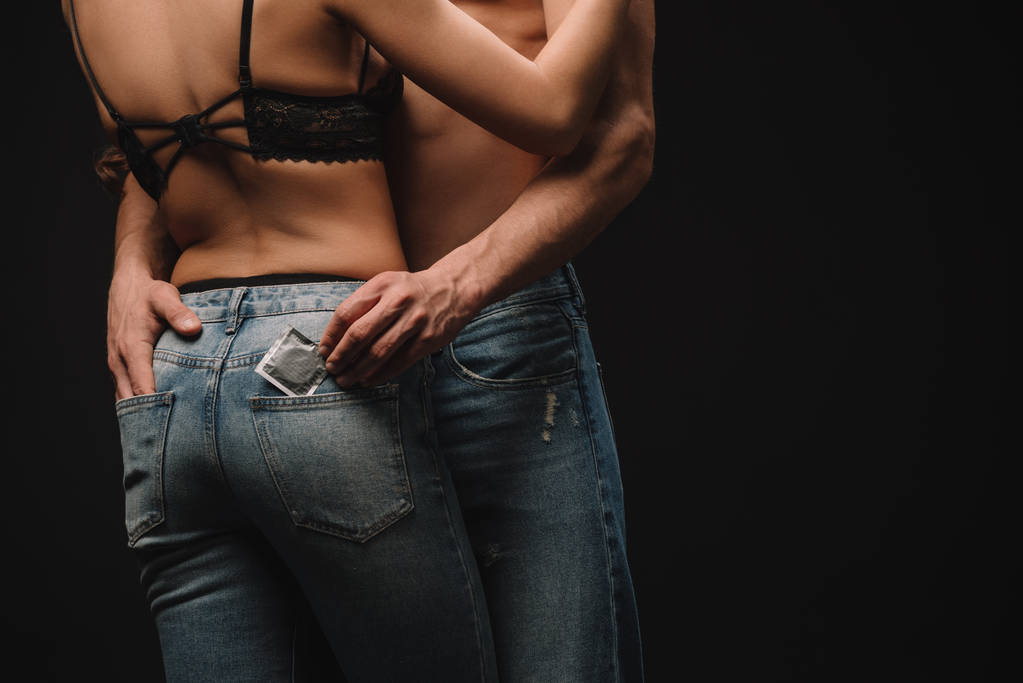 обрізаний вид чоловіка обіймає жінку і тримає презерватив ізольовано на чорному
 - Фото, зображення