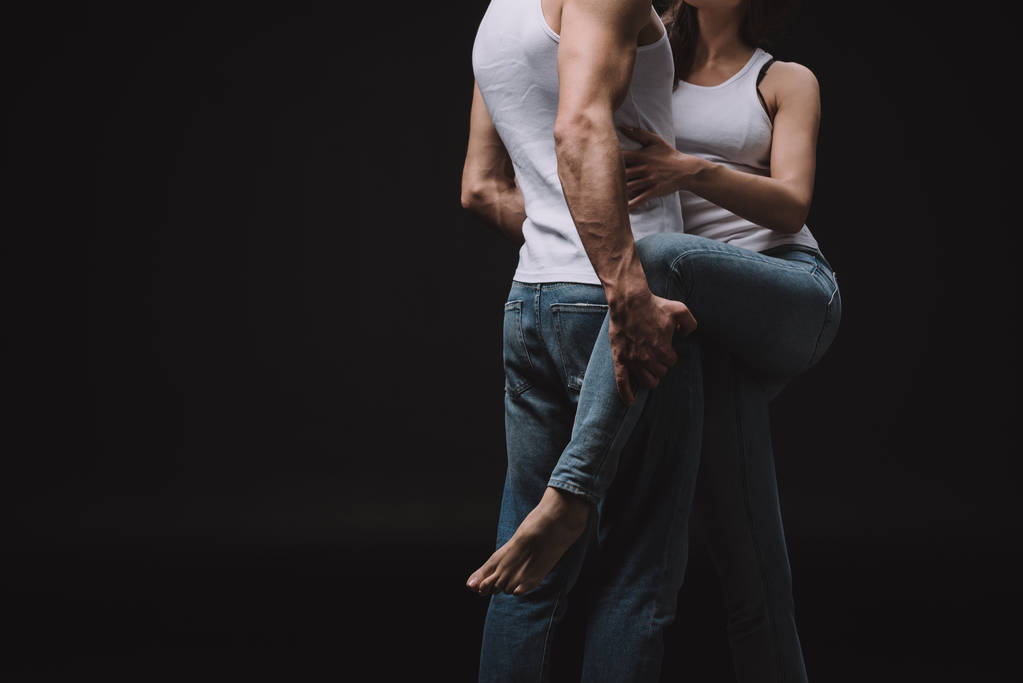 vista cortada de casal abraçando em singlets brancos e jeans isolados em preto
 - Foto, Imagem
