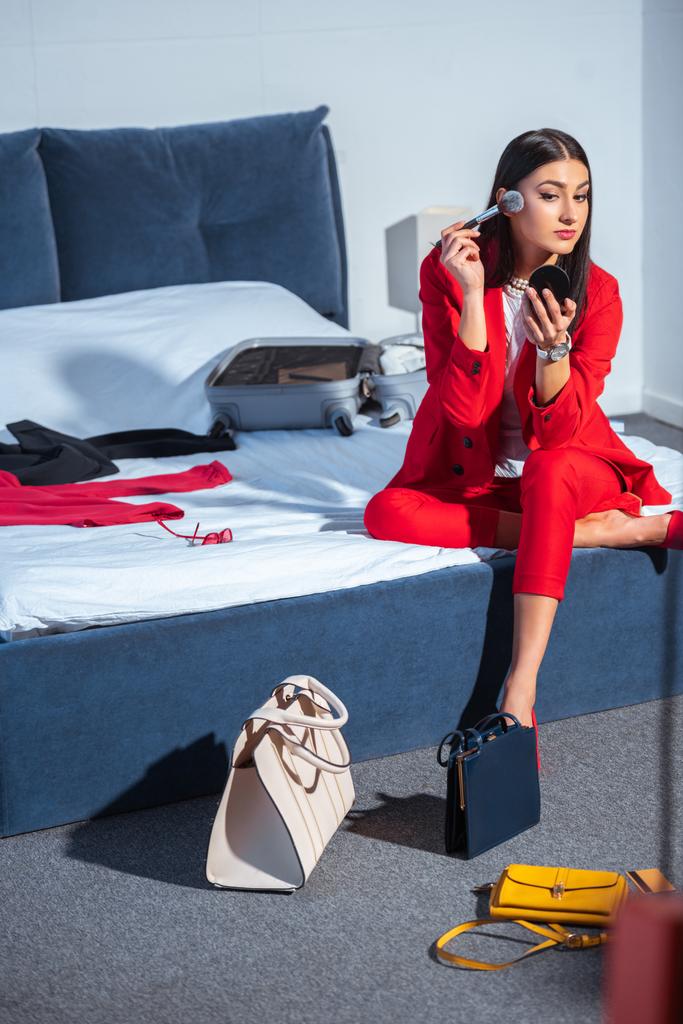 красивая стильная молодая женщина сидит на кровати и наносит макияж
  - Фото, изображение
