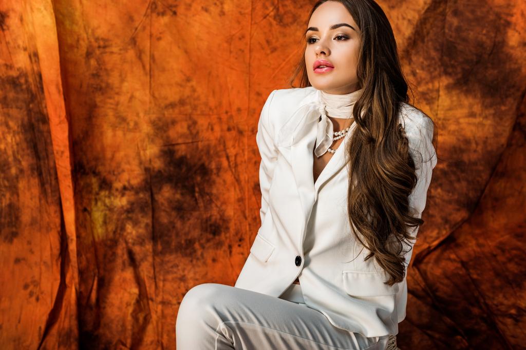 attractive girl with long brown hair in white suit posing on chair on textured background - Photo, Image