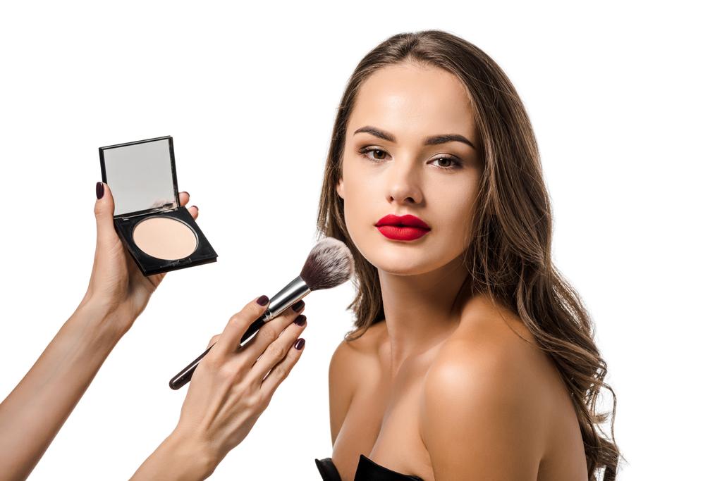 visão recortada da mulher aplicando pó com escova cosmética no rosto do belo modelo olhando para a câmera isolada no branco
 - Foto, Imagem