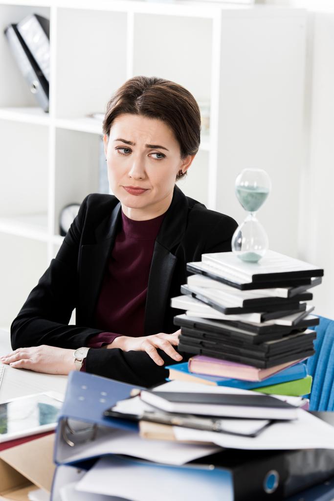 aantrekkelijke triest zakenvrouw kijken zandloper in kantoor - Foto, afbeelding