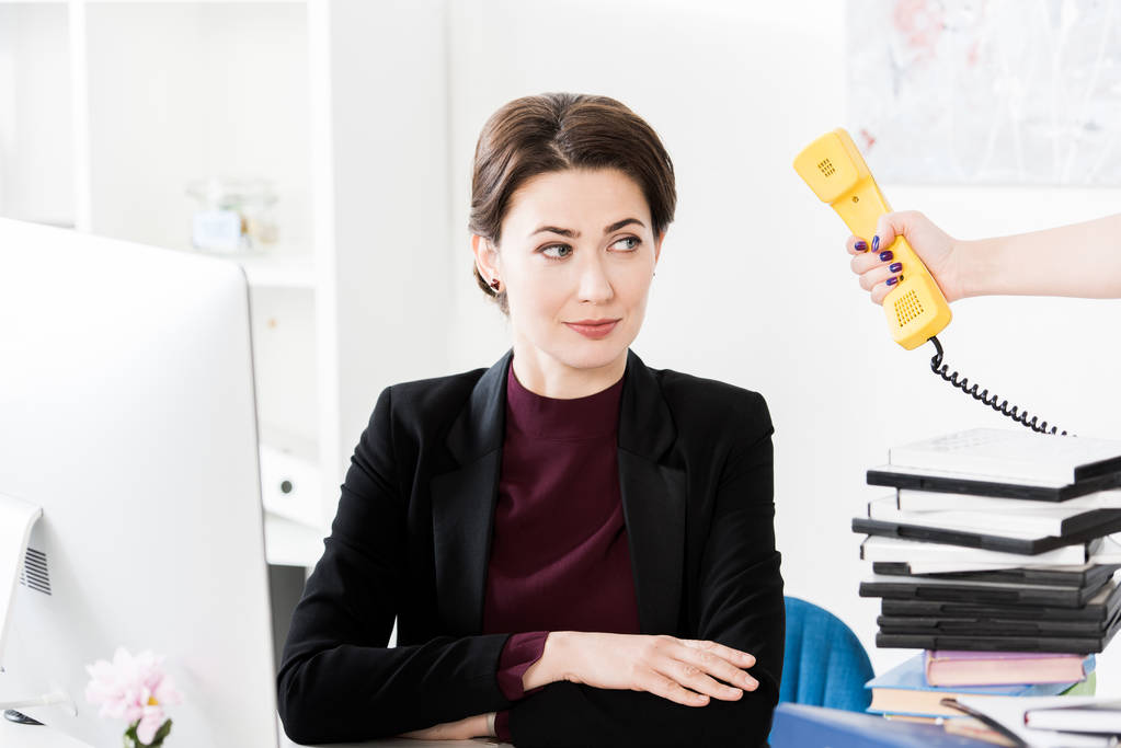 секретарка, що дає жовтий стаціонарний телефон красивій бізнес-леді в офісі
 - Фото, зображення