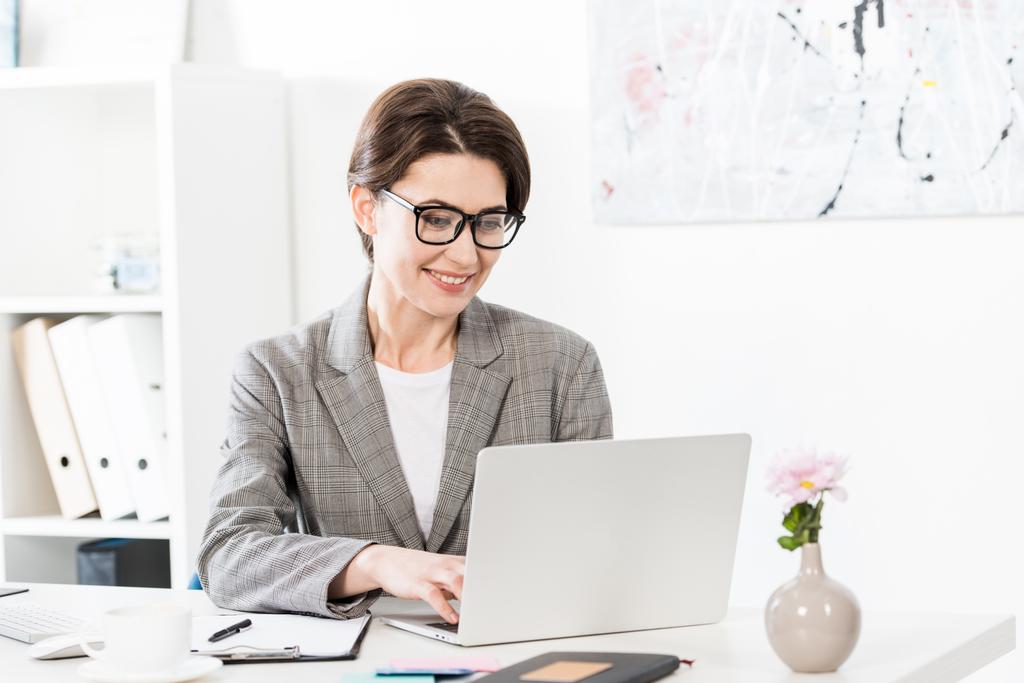 sorridente atraente empresária usando laptop no escritório
 - Foto, Imagem