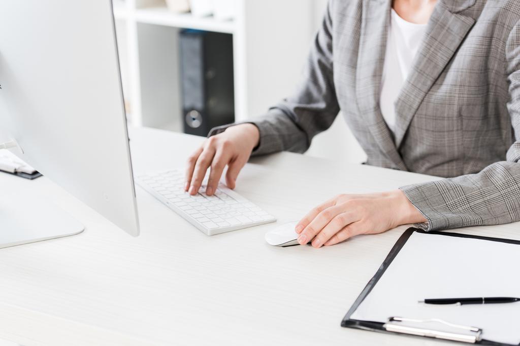 immagine ritagliata di donna d'affari in abito grigio seduta con computer in ufficio
 - Foto, immagini
