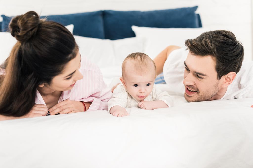 Porträt junger Eltern mit kleinem Baby, das zu Hause zusammen im Bett liegt - Foto, Bild