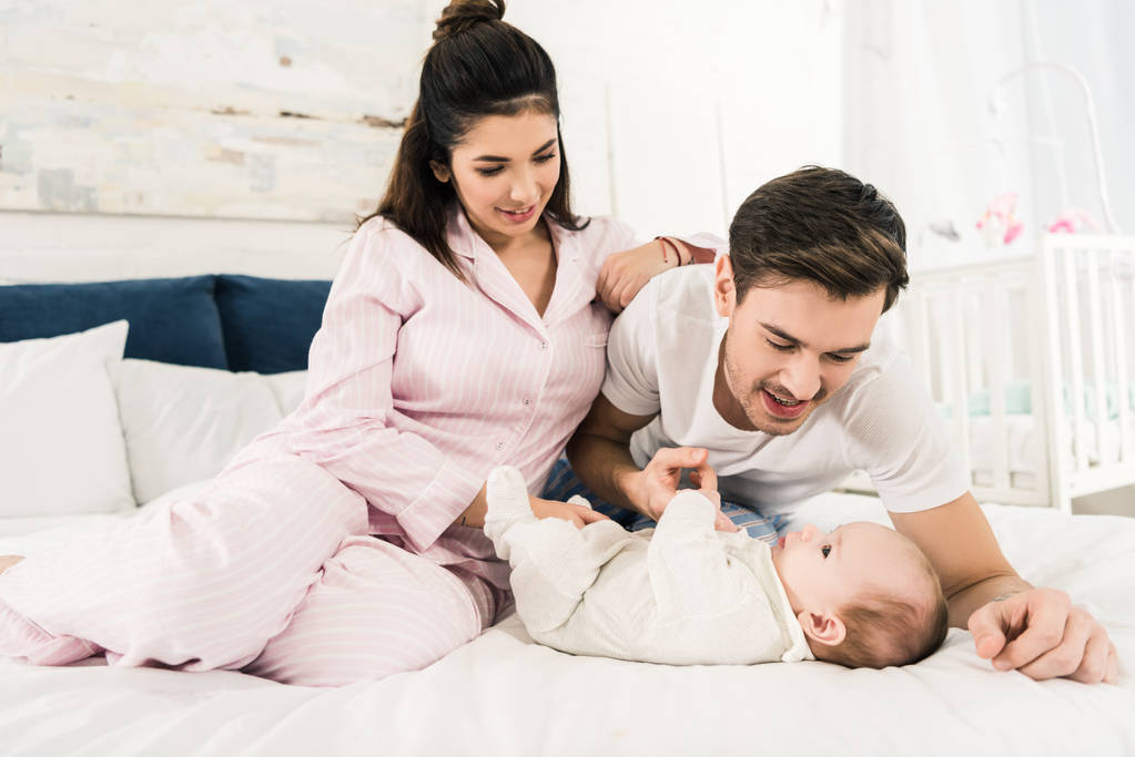 onnelliset vanhemmat lepäävät sängyssä yhdessä söpön vauvan kanssa kotona
 - Valokuva, kuva