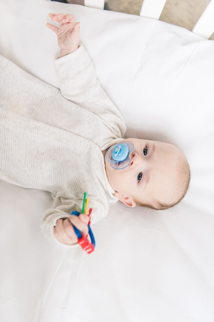 overhead view of little baby with pacifier holding toy while lying in crib - Photo, Image