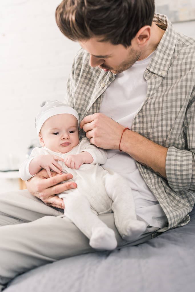 jonge man met babyjongen in handen thuis - Foto, afbeelding