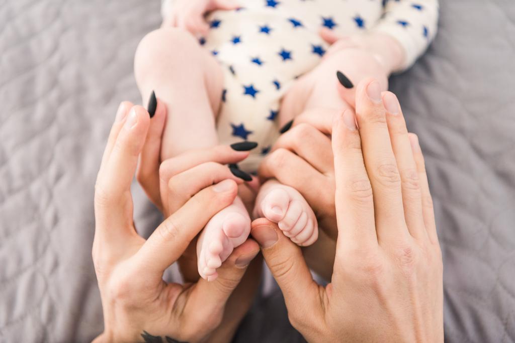vista parcial de los padres sosteniendo pequeños pies de bebé en las manos juntas
 - Foto, Imagen