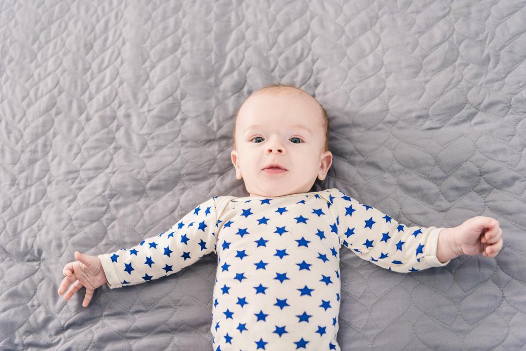 над головой вид очаровательного маленького ребенка, лежащего на сером одеяле
 - Фото, изображение