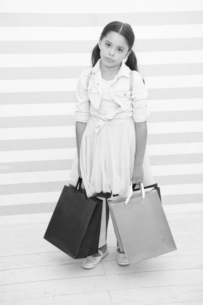 Einkaufen ermüdende anstrengende Tätigkeit. Kind trägt Einkaufstaschen gestreift Hintergrund. Mädchen verbringen den Tag damit, Dinge für die Schule zu kaufen. Zurück zur Schulverkaufszeit. Mädchen hält erschöpft Tüten - Foto, Bild