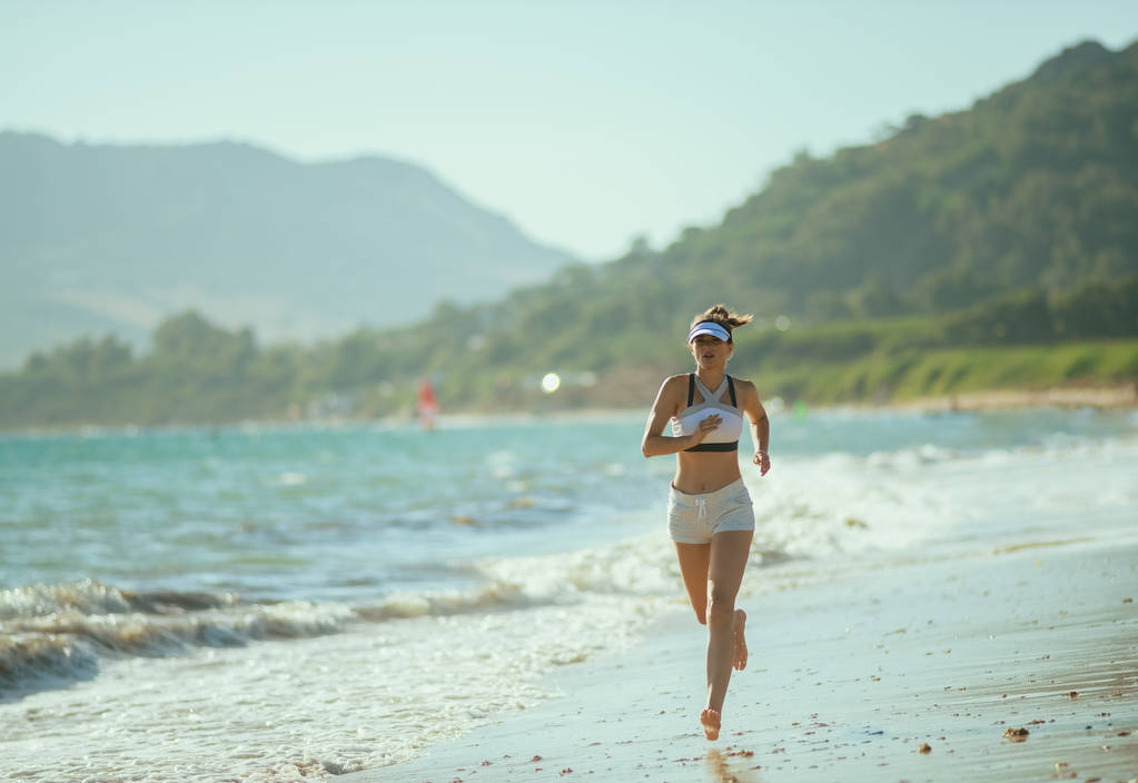 mujer sana corredora en ropa deportiva en la costa por la noche corriendo. viaje a la costa para hacer ejercicio al aire libre impacta positivamente en el cuerpo humano. Manténgase saludable y sienta el control total de su vida
 - Foto, imagen