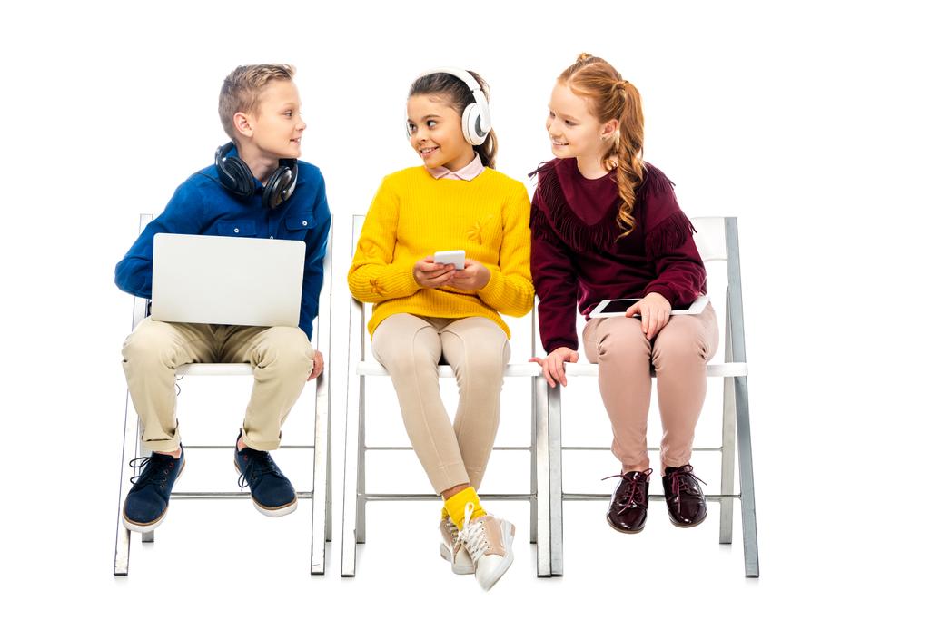 милі школярки з цифровими пристроями дивиться на хлопчика з ноутбуком ізольовані на білому
 - Фото, зображення