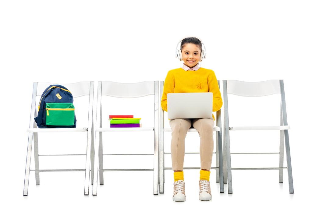 hymyilevä koulutyttö kuulokkeet päähän istuu tuolilla, pitämällä kannettavaa tietokonetta ja katsomalla kameraa eristetty valkoinen
 - Valokuva, kuva