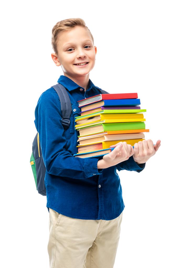 cute boy with backpack holding stack of books and looking at camera isolated on white - Photo, Image