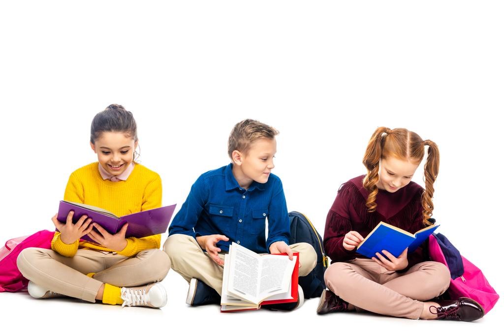 χαρούμενα παιδιά σχολικής ηλικίας, καθισμένος και ανάγνωση βιβλίων που απομονώνονται σε λευκό - Φωτογραφία, εικόνα