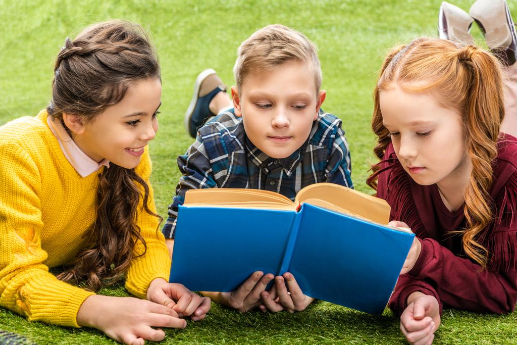 かわいい子供たちの芝生の上で横になっていると、本を読んで - 写真・画像