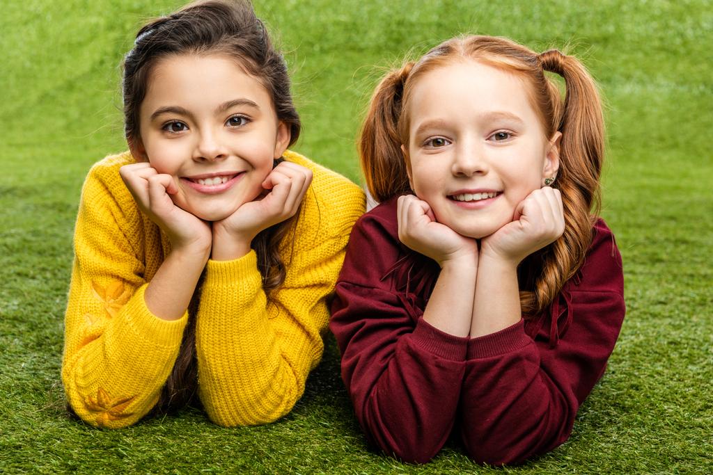 smiling schoolgirls lying on lawn and looking at camera - Photo, Image