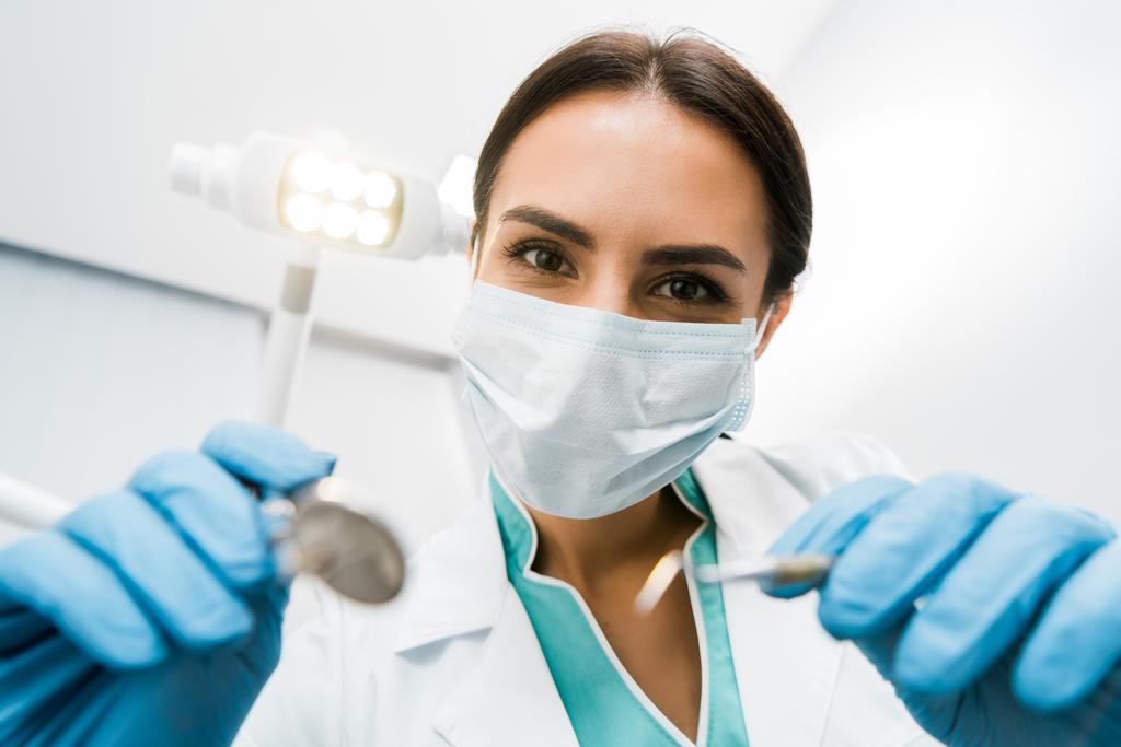 вибірковий фокус жінки-стоматолога в масці, що тримає інструменти в руках
 - Фото, зображення