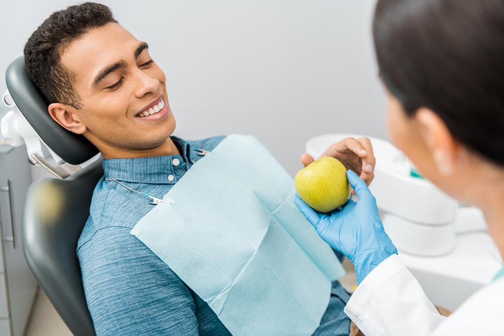 femaledentist giving apple to handsome african american patient  - Photo, Image