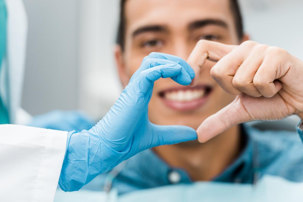 selectieve aandacht van tandarts en Afrikaanse Amerikaan patiënt handen waardoor hart vorm  - Foto, afbeelding
