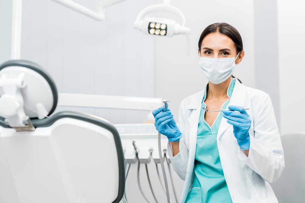 γυναίκα οδοντίατρος στο λευκό παλτό και μάσκα κρατώντας οδοντιατρική μέσα  - Φωτογραφία, εικόνα