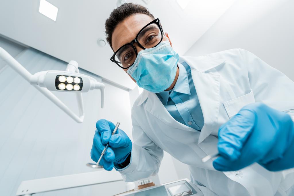 stomatologue afro-américain en lunettes et masque avec des instruments dentaires dans les mains
 - Photo, image
