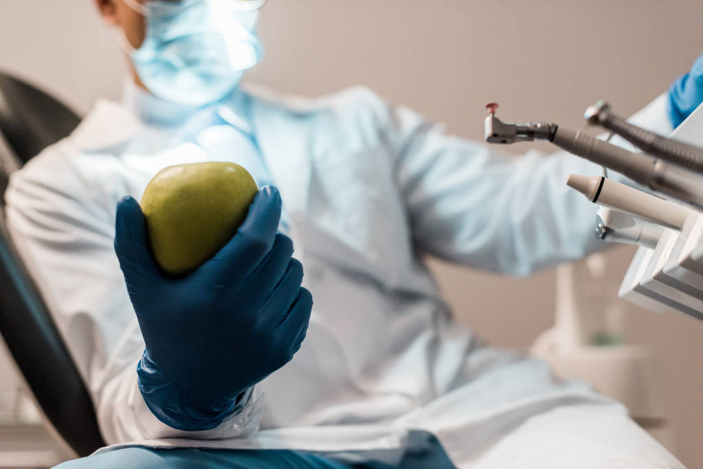 abgeschnittene Ansicht eines Apfels in der Hand eines männlichen Zahnarztes mit Latexhandschuhen  - Foto, Bild