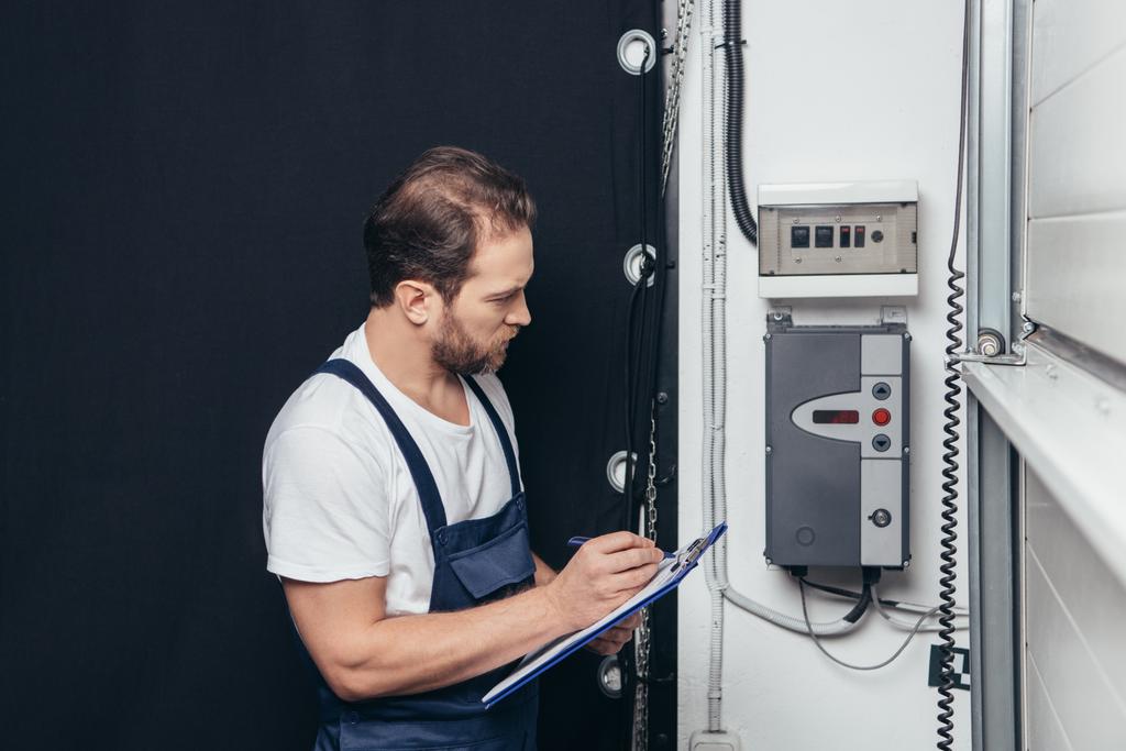 male electrician writing in clipboard and checking electrical box  - Photo, Image