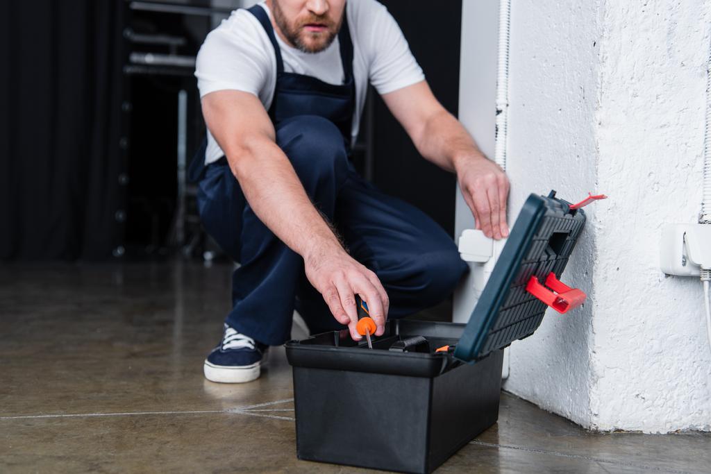 обрезанное изображение электрика-мужчины, вынимающего отвертку из ящика с инструментами во время ремонта розетки
  - Фото, изображение