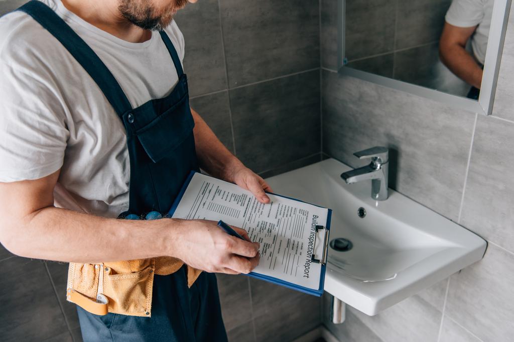 vista parziale dell'idraulico maschio con la scrittura della cintura degli attrezzi negli appunti vicino al lavandino rotto in bagno
 - Foto, immagini