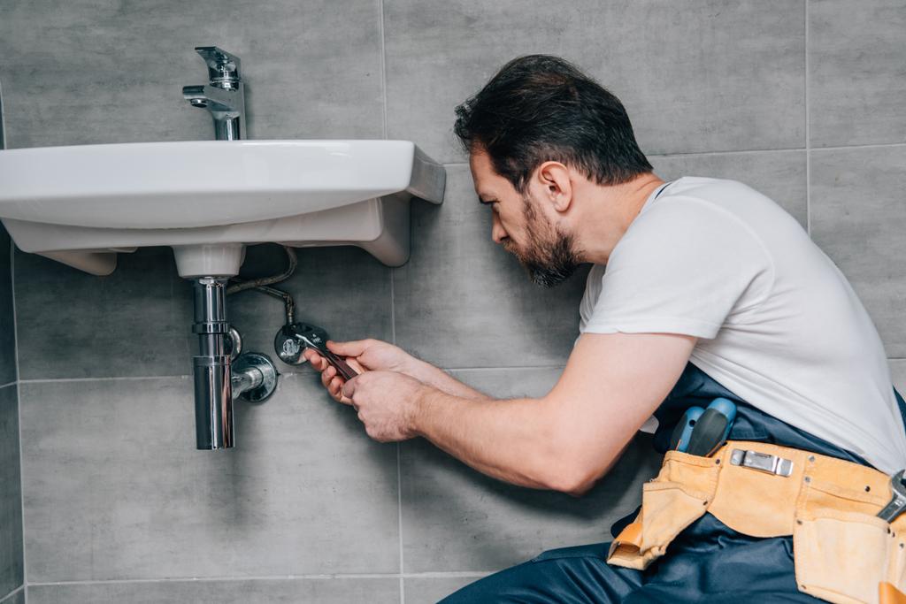 vista lateral do encanador masculino no trabalho pia de fixação geral por chave na casa de banho
  - Foto, Imagem