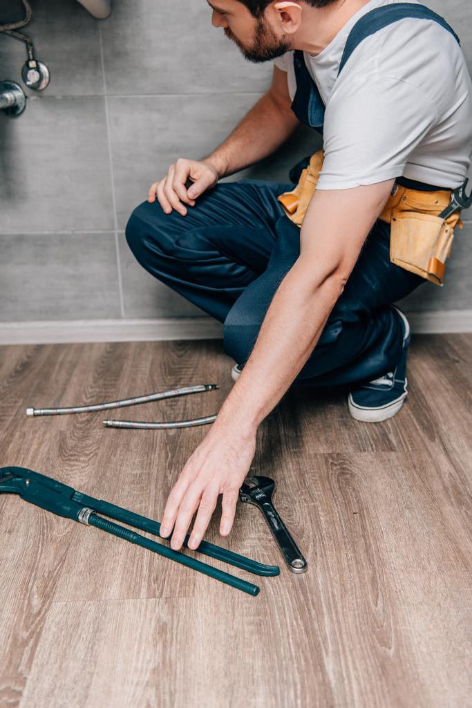 visão parcial do encanador masculino que toma a chave de gás para reparar o dissipador quebrado no banheiro
  - Foto, Imagem