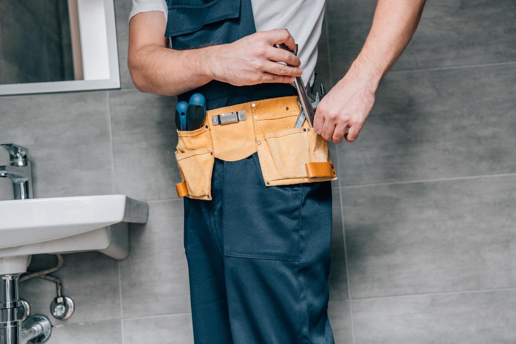 ritagliato colpo di idraulico maschio mettendo chiave in cintura degli attrezzi in bagno
  - Foto, immagini
