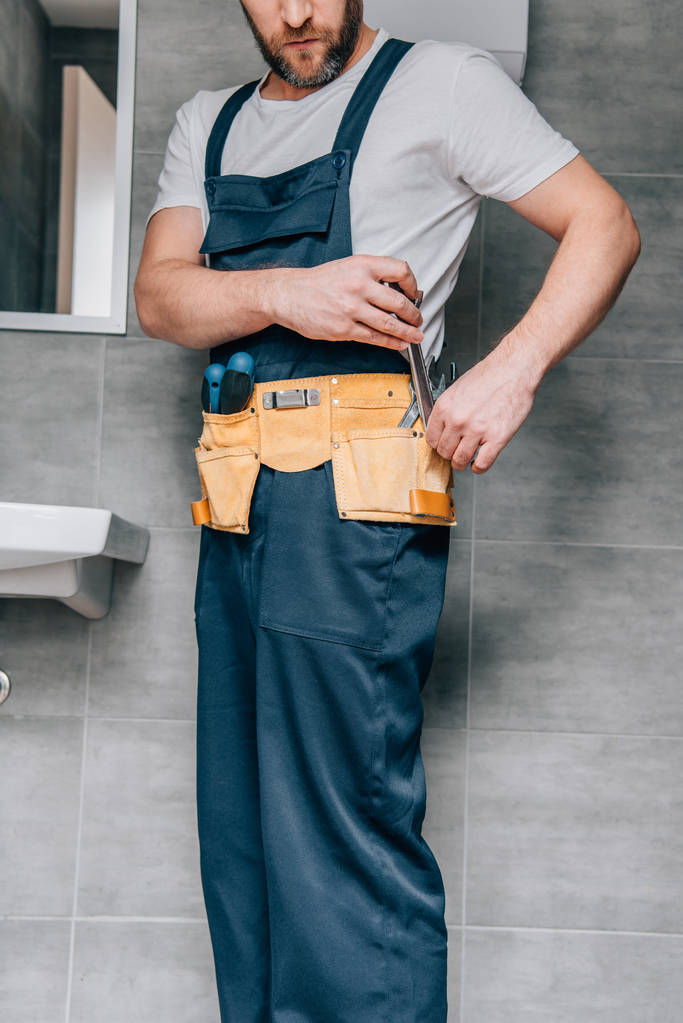férfi vízvezeték-szerelő, üzembe csavarkulcs toolbelt fürdőszobában részleges megtekintése  - Fotó, kép