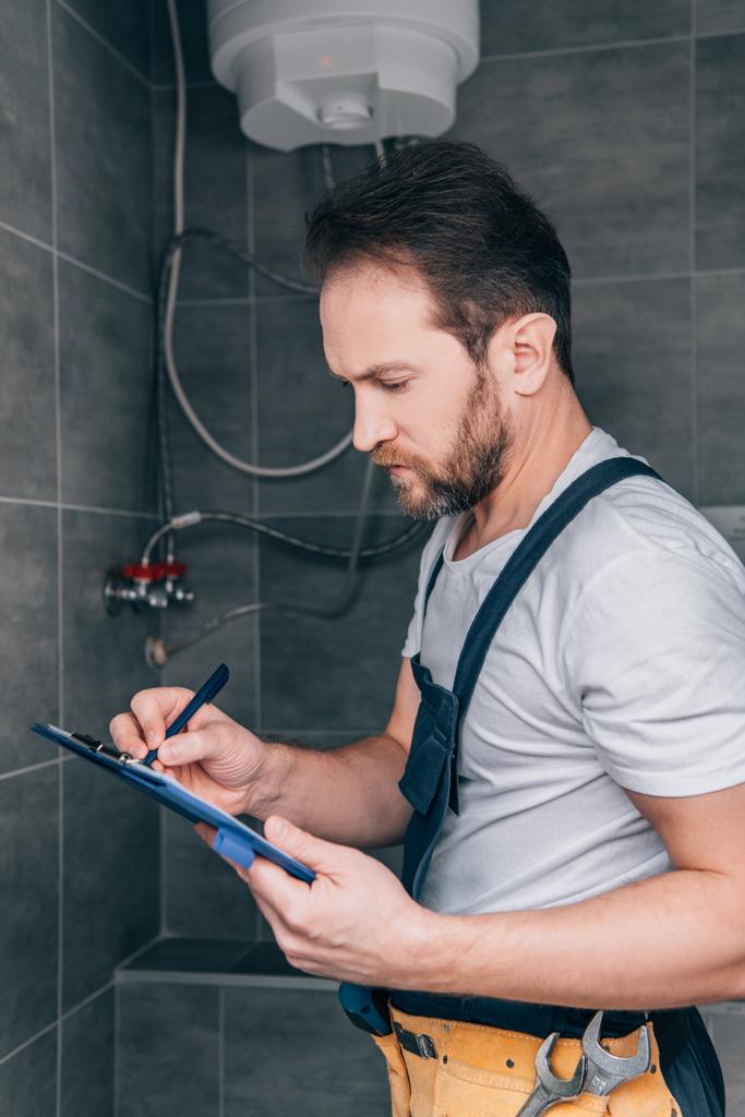 взрослый сантехник пишет в буфер обмена и проверяет электрический котел в ванной комнате
  - Фото, изображение