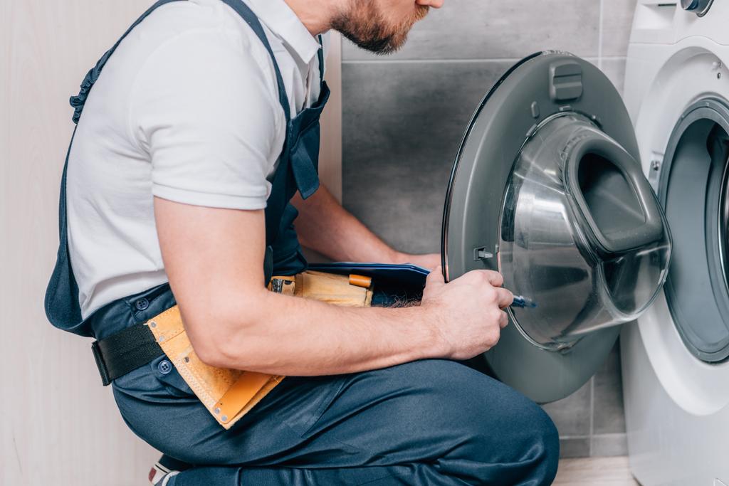 Oříznout záběr údržbář s toolbelt a schránky kontrola pračka v koupelně - Fotografie, Obrázek