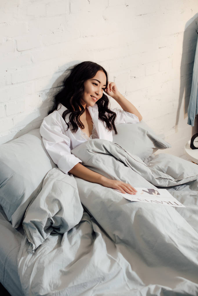 Blick aus der Vogelperspektive auf die schöne lächelnde junge Frau, die mit Reisezeitung im Bett liegt - Foto, Bild