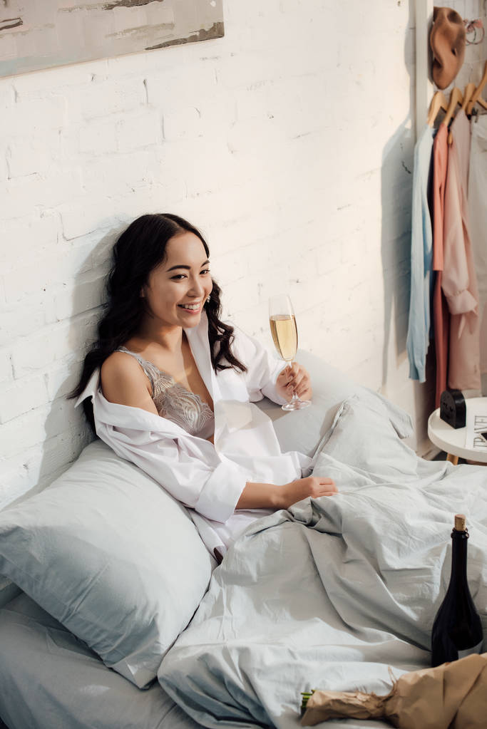 high angle view of beautiful happy asian girl drinking wine in bed - Photo, Image