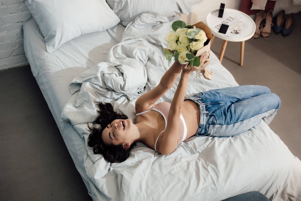 high angle view of beautiful happy asian girl lying on bed and holding bouquet of flowers - Photo, Image