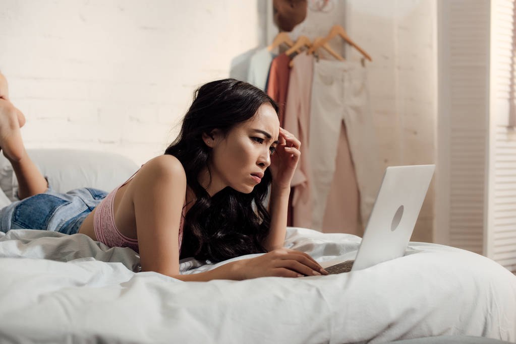 vakava frowning nuori nainen käyttää kannettavaa tietokonetta sängyssä
 - Valokuva, kuva