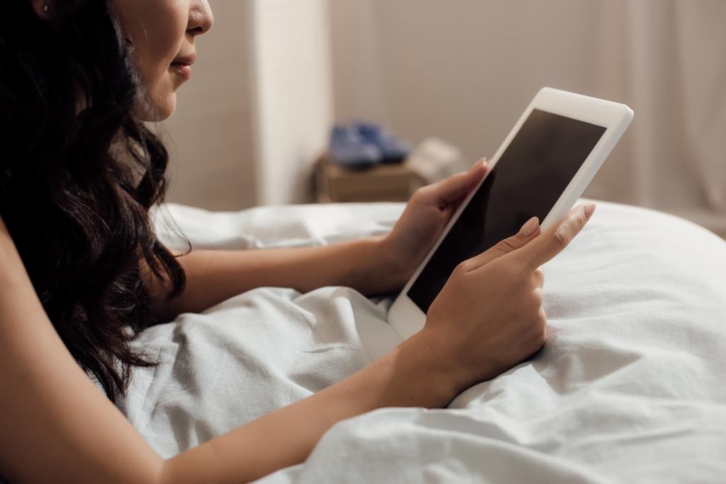 abgeschnittene Aufnahme eines attraktiven Mädchens, das auf dem Bett liegt und ein digitales Tablet mit leerem Bildschirm benutzt - Foto, Bild