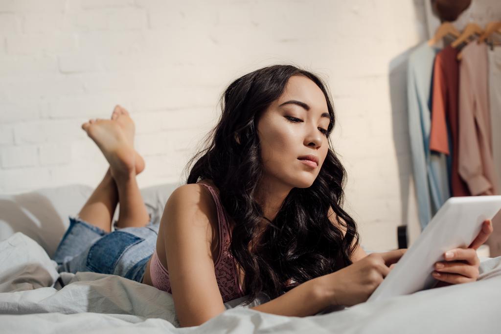 красива молода жінка лежить на ліжку і використовує планшетний ПК
 - Фото, зображення
